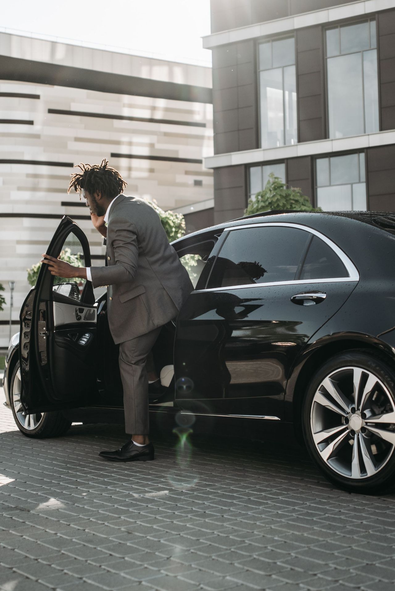 Professional chauffeur in a tailored suit opening the door of a black luxury vehicle for a client